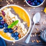 Wandbild: Mango-Smoothies-Schüssel mit Blaubeeren, Müsli, Chiasamen